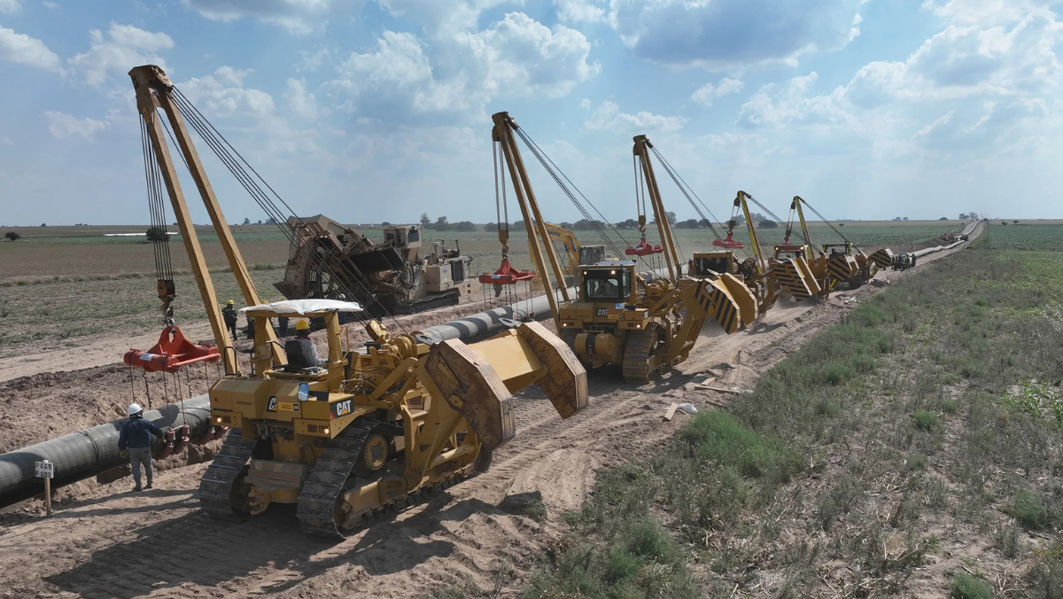 Pipeline construction crews using heavy machinery to position large pipeline sections