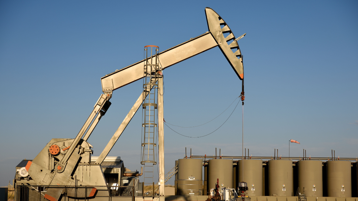 Oil pumpjack operating near storage tanks under clear sky in Vaca Muerta shale field