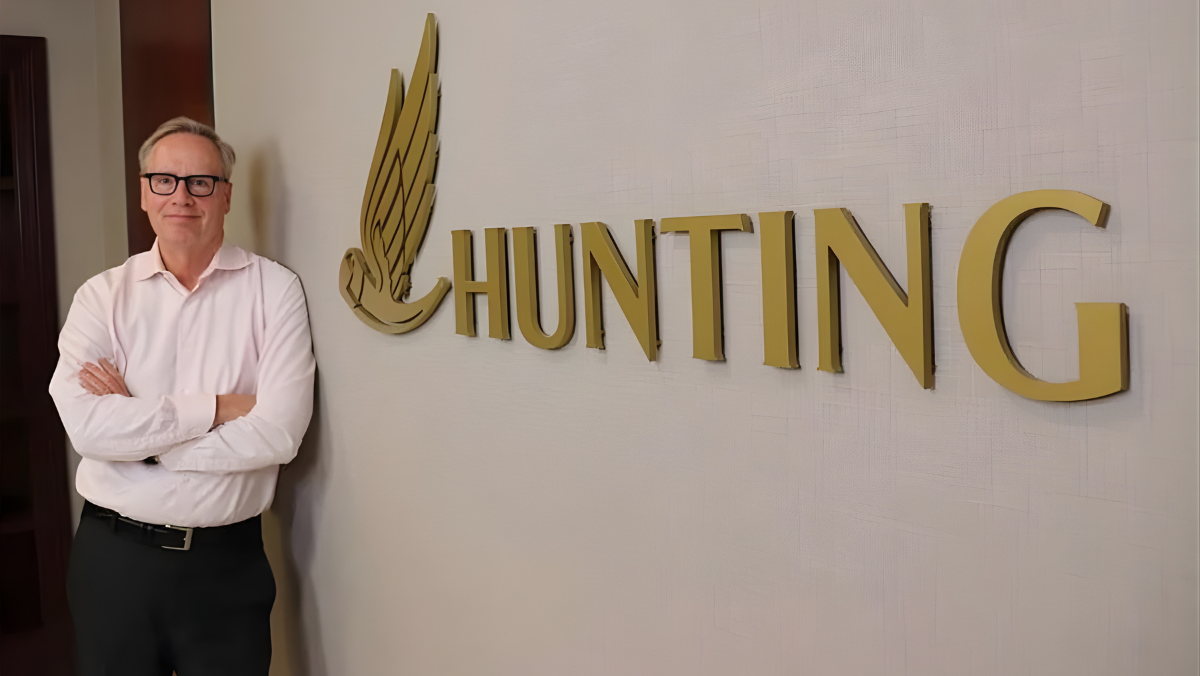 Executive standing beside Hunting Energy Services logo inside corporate office