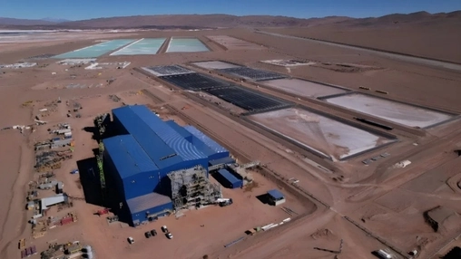 Aerial view of a large mining facility under construction in an arid desert landscape with evaporation ponds